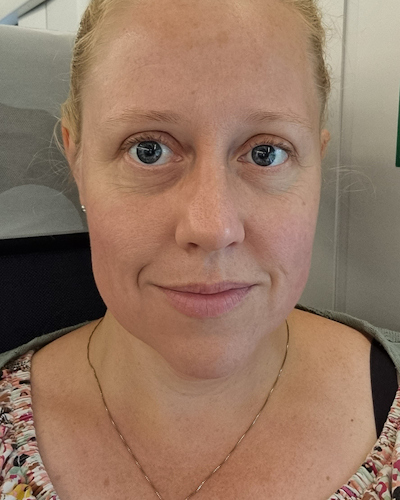Kvinna med blont hår sitter i en stol och tittar rakt in i kameran.