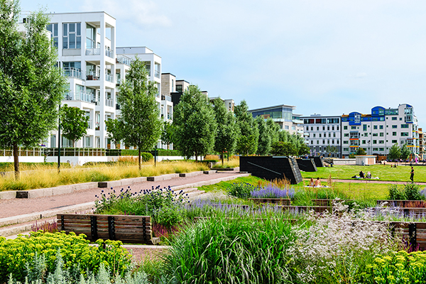Moderna bostadsbyggnader och en park med gångvägar, växter och människor som kopplar av en soldag.