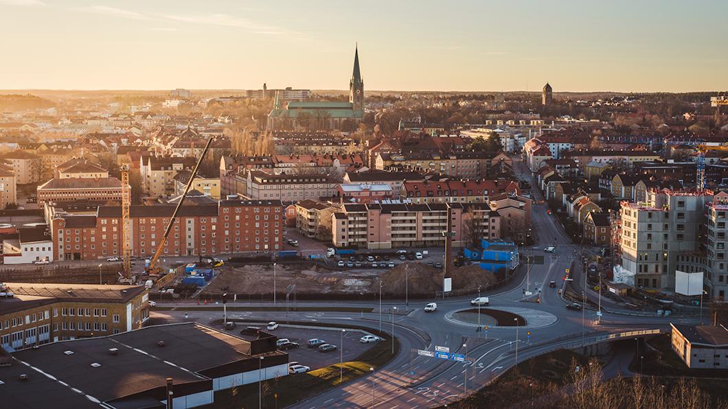 Stadsvy från ovan där en kyrka med hög spira, bostadshus, vägar och fordon syns.