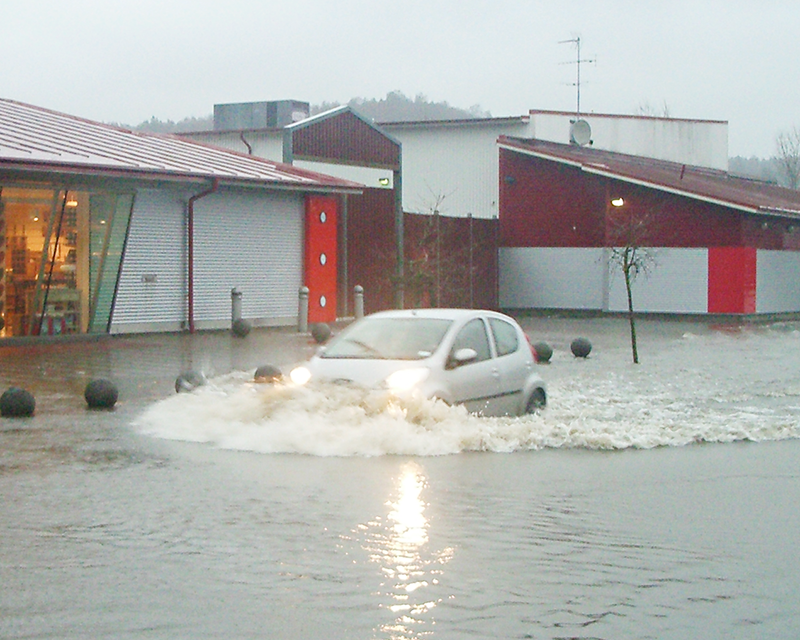 En bil kör genom ett översvämmat område.