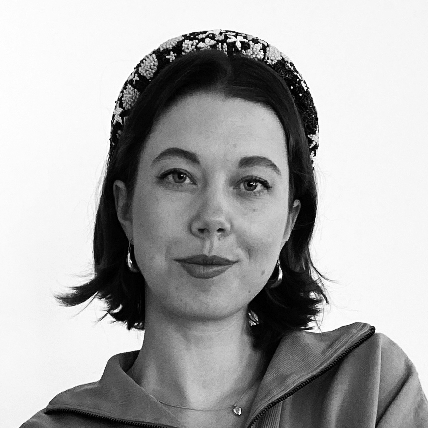 Porträtt i svartvitt av en kvinna med kort hår. Hon har ett mönstrat hårband, ringörhängen, ett halsband och en topp med dragkedja. Hon ser in i kameran med neutral min.