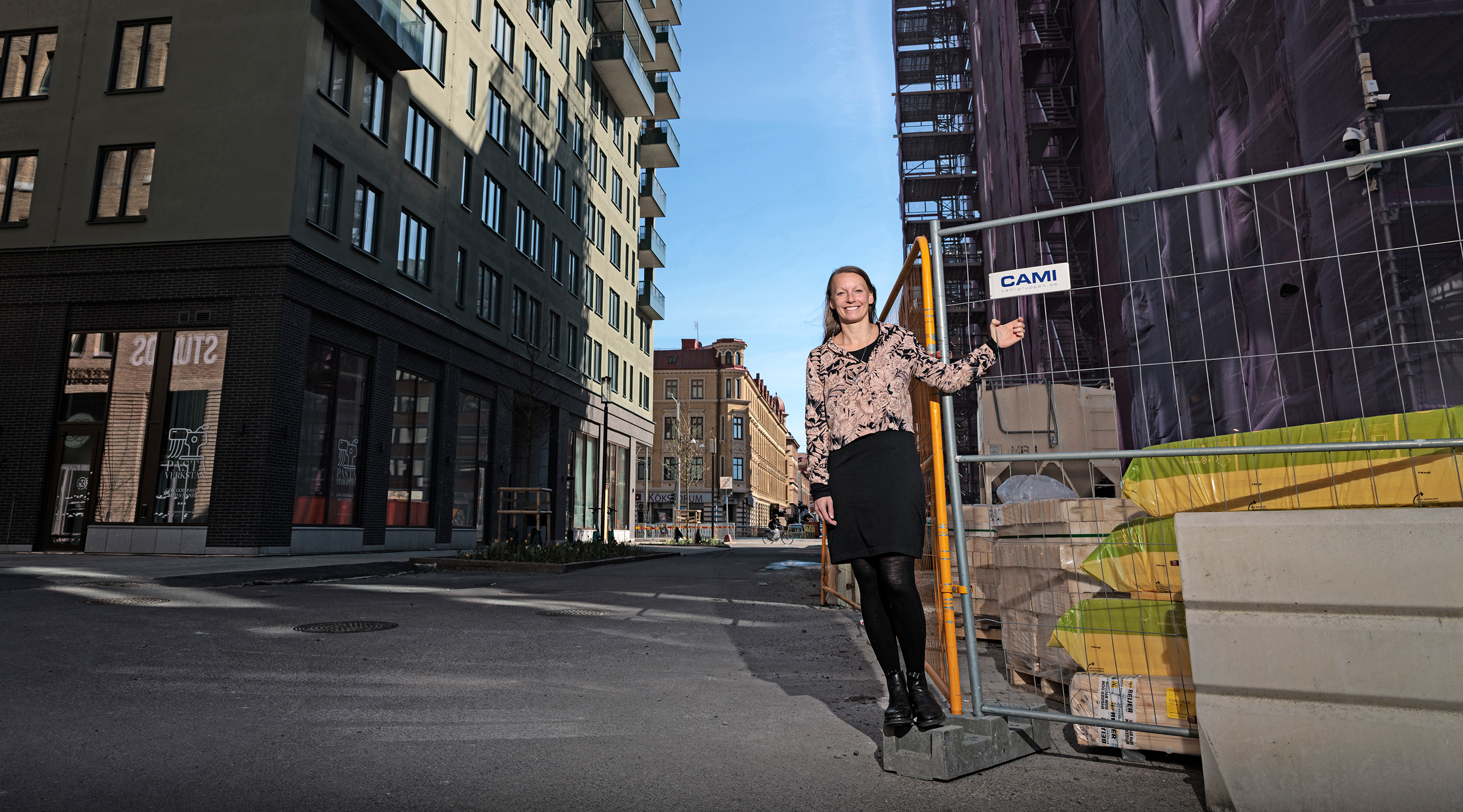 En kvinna står bredvid ett byggstängsel på en stadsgata och pekar på en skylt med texten "CAMI".