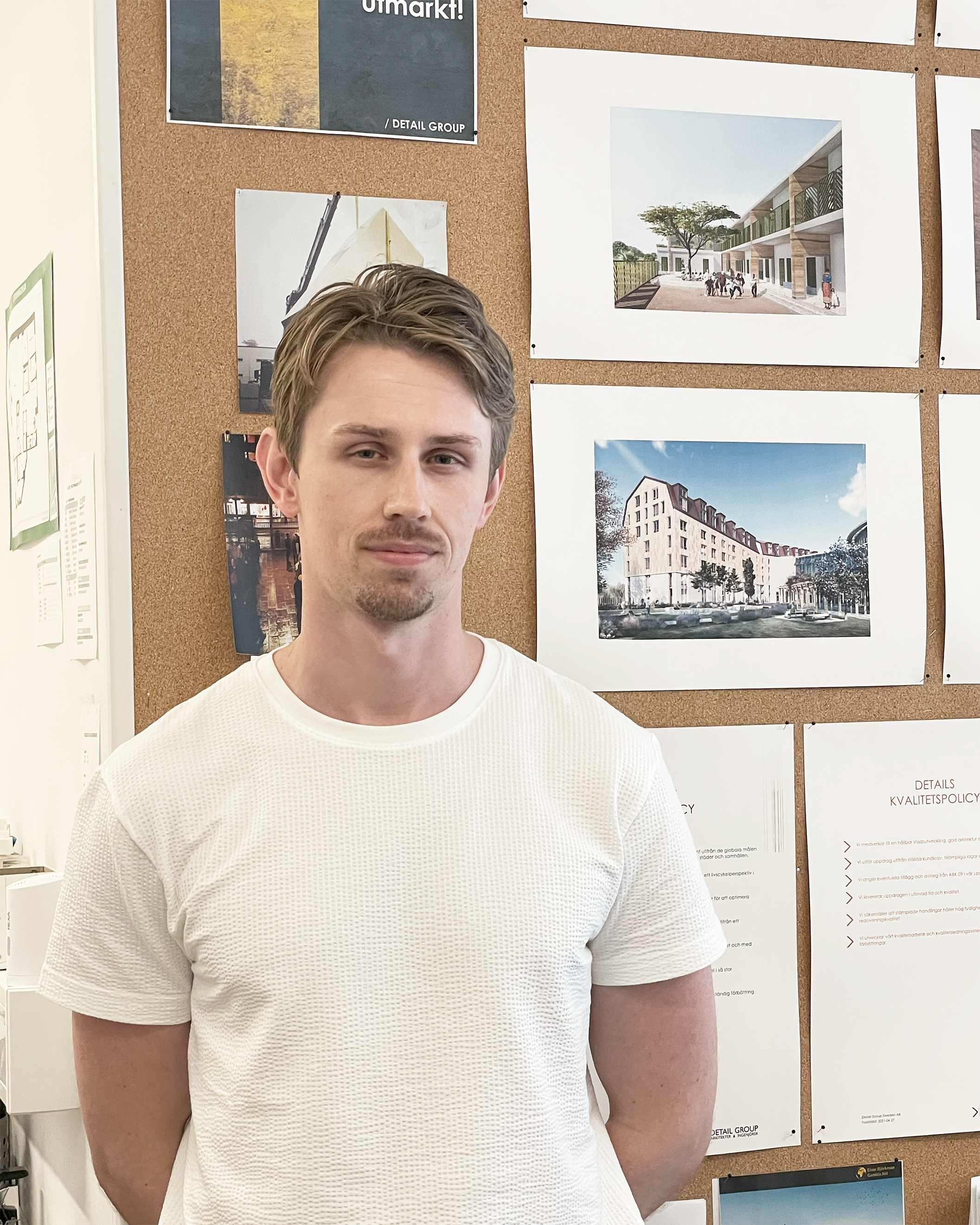 En man i vit skjorta står framför en anslagstavla med arkitektritningar och bilder.