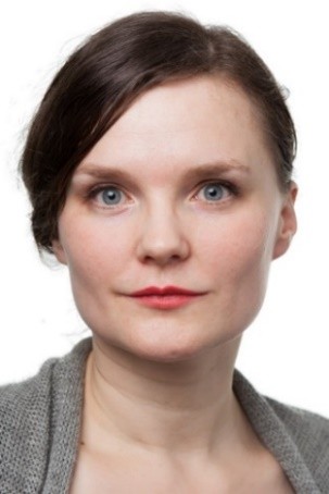 Kvinna med blå ögon och brunt bakåtdraget hår, har grå tröja och ser mot kameran framför vit bakgrund.