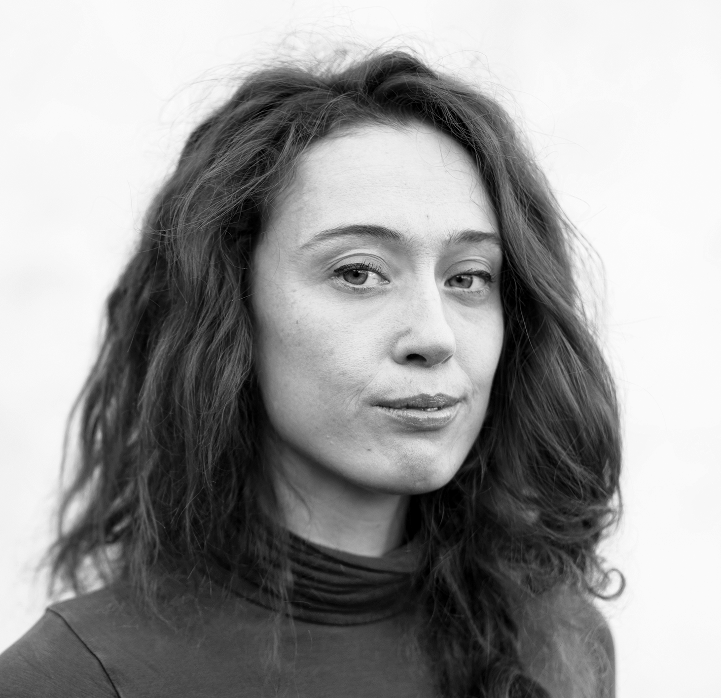 Svartvit porträttbild av en kvinna med vågigt hår och hög krage, som tittar lite åt sidan med neutral min.