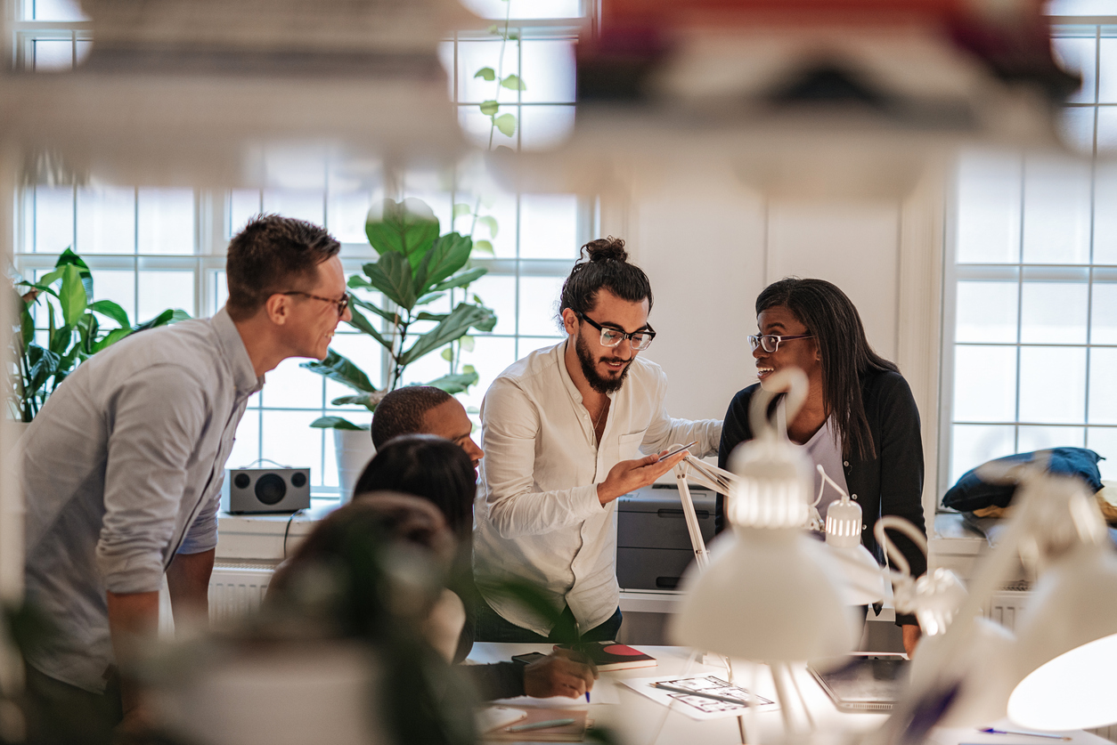 En grupp kollegor sitter runt ett bord på ett kontor och diskuterar tillsammans med dokument i händerna.