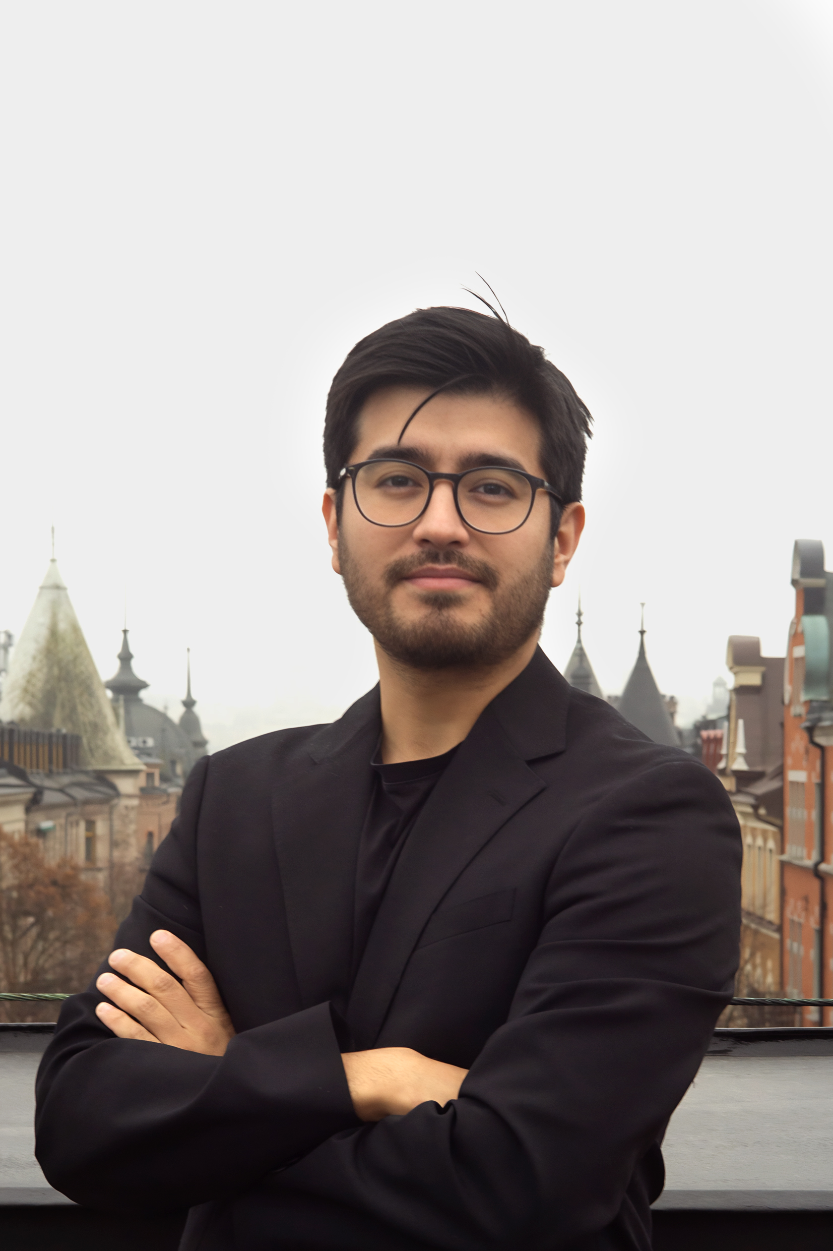 En man i svart kavaj står med armarna i kors på ett tak, med europeiska byggnader i bakgrunden under molnig himmel.