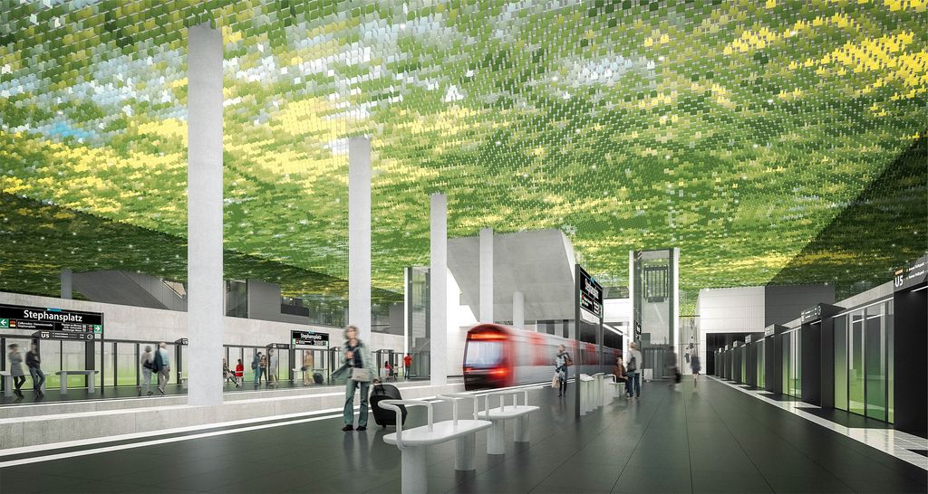 Tågstation med gröna takplattor, glasväggar, bänkar och ett rött tåg vid plattformen; personer står och går.