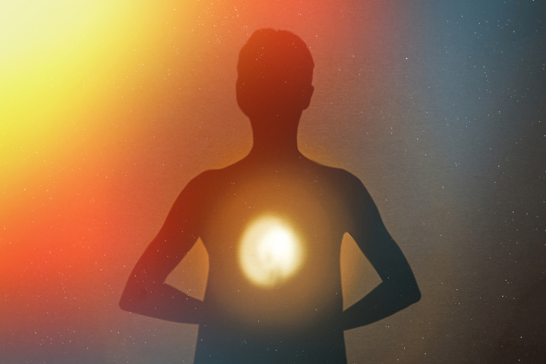 Siluett av en person med händerna på höfterna, ett starkt ljus vid bröstet och en bakgrund med flera färger.