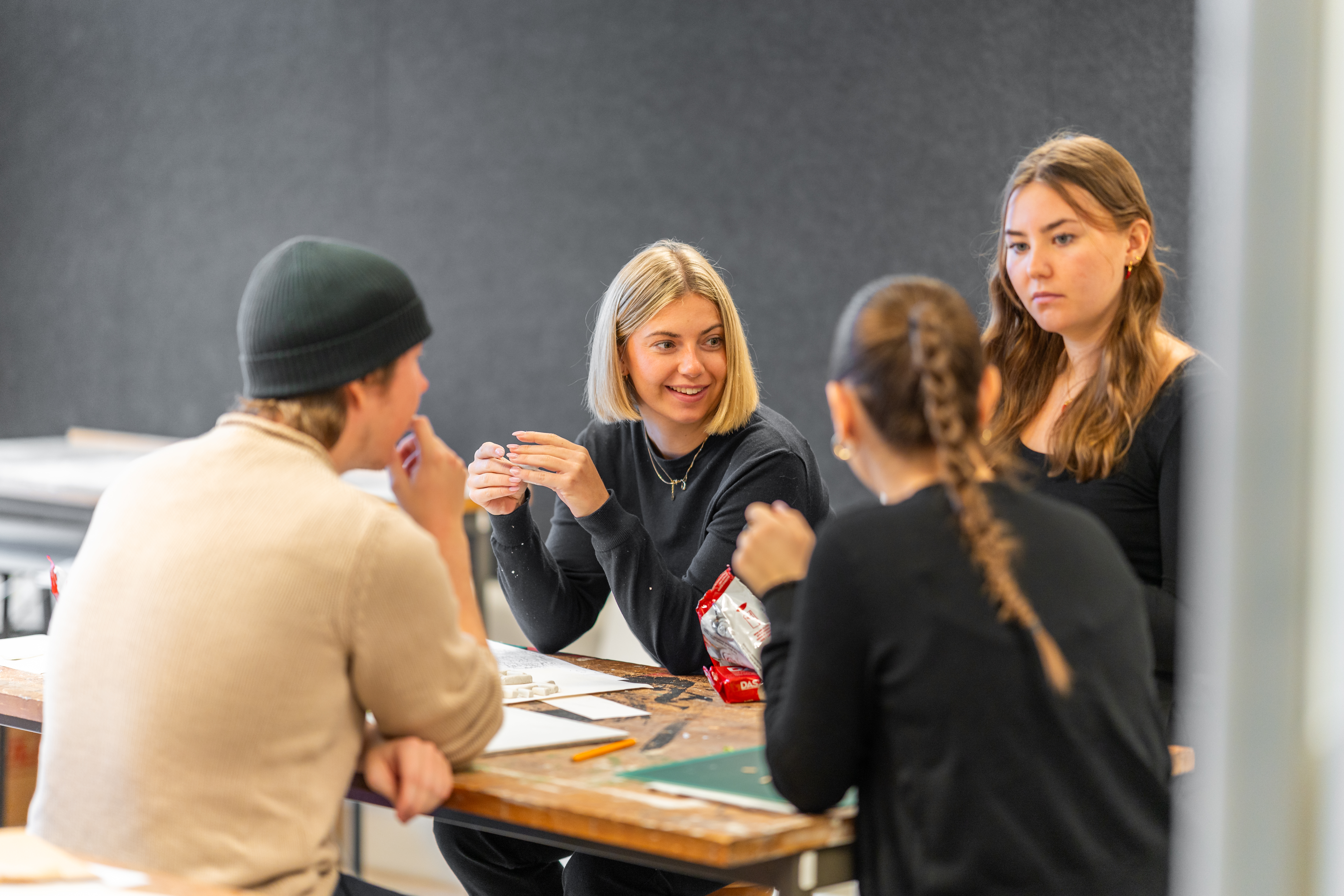 Fyra personer sitter runt ett bord och samtalar, med papper och snacks framför sig i ett rum med bra belysning.