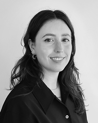 En kvinna med långt mörkt hår och en mörk skjorta tittar in i kameran mot en ljus bakgrund.