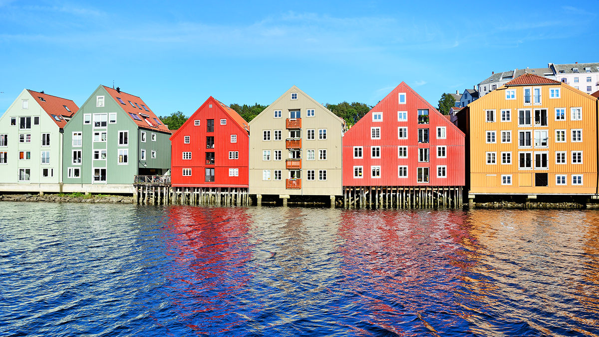 Trähus på pålar står vid vattnet och speglar sig i vattnet under en delvis molnig himmel.