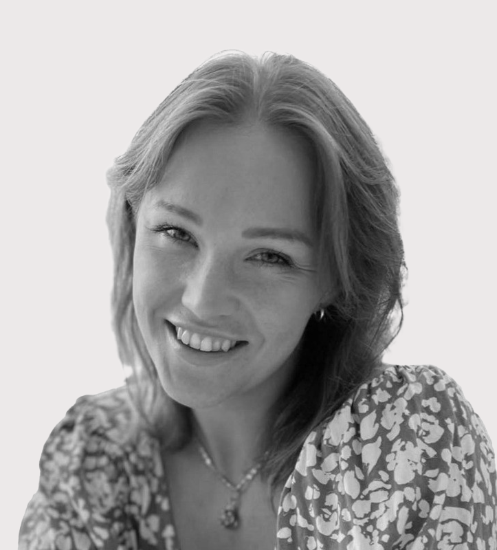 En kvinna med axellångt hår ler mot kameran, har på sig en mönstrad topp och ett halsband mot en enkel bakgrund.