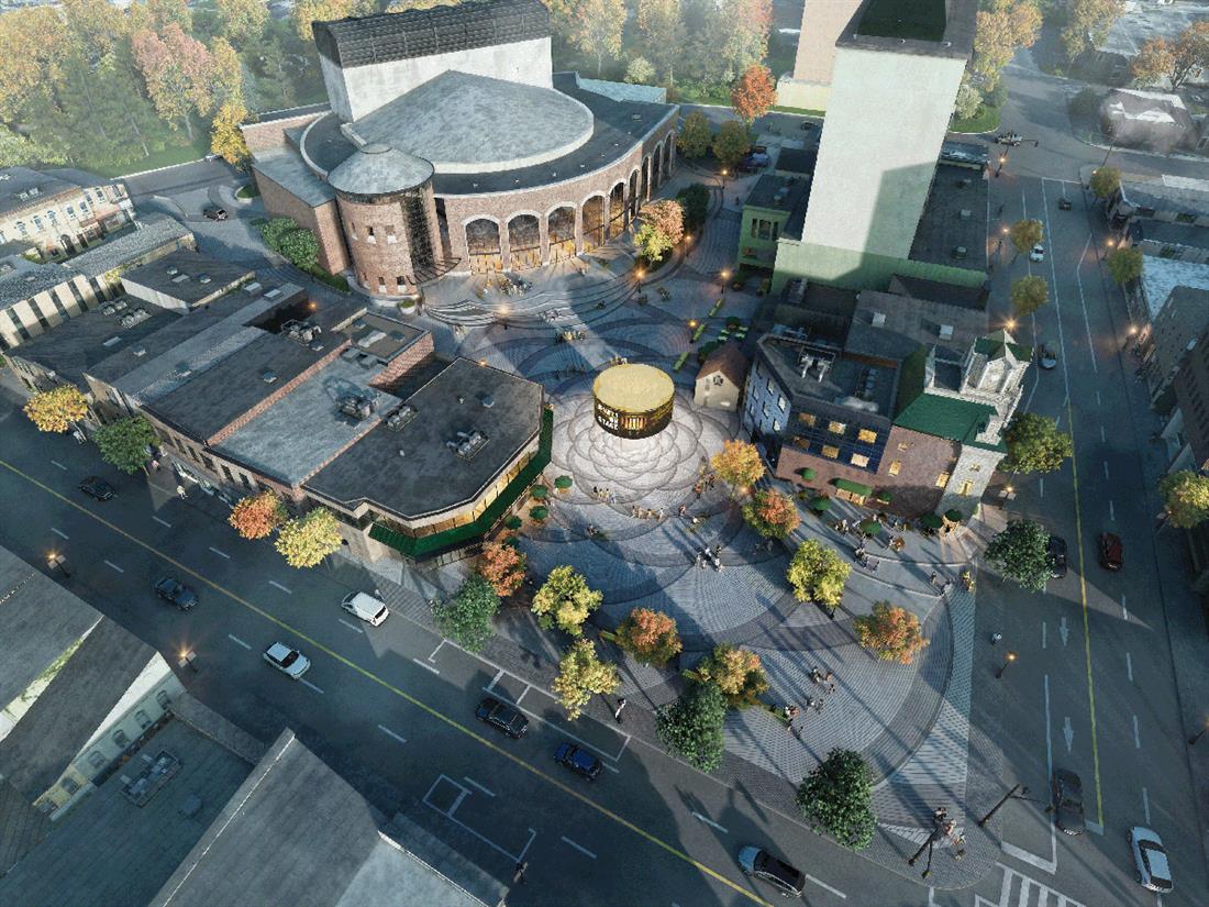 Flygbild av ett stadsplan med en cirkelformad byggnad i mitten, omgiven av byggnader, gator och några träd.