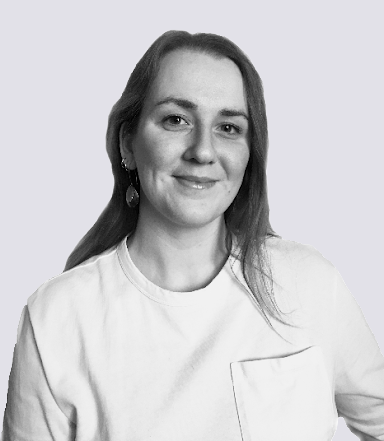 En kvinna med långt hår och en ljus skjorta ler och står mot en ljus bakgrund.