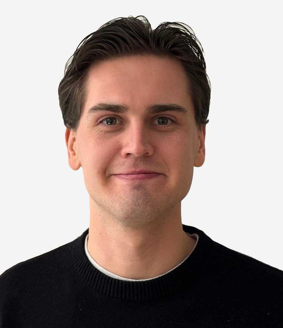En ung man med kort brunt hår, svart tröja över en ljusgrå skjorta, ser in i kameran mot en vit bakgrund.