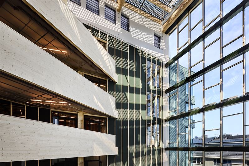 En vy inifrån ett byggnadsatrium med stora glasfönster, synliga konstruktionselement och skuggor på väggarna.