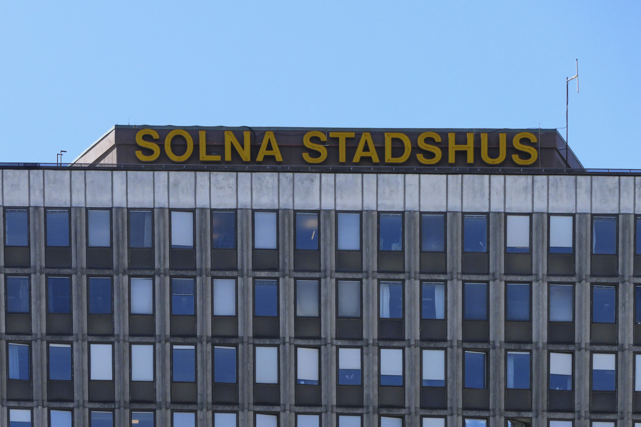 De översta våningarna av en kontorsbyggnad med skylten "Solna Stadshus" i gula bokstäver mot himlen.
