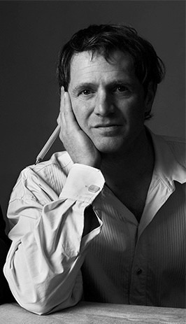 Person i skjorta med krage vilar huvudet i ena handen, håller en penna och tittar rakt mot kameran.