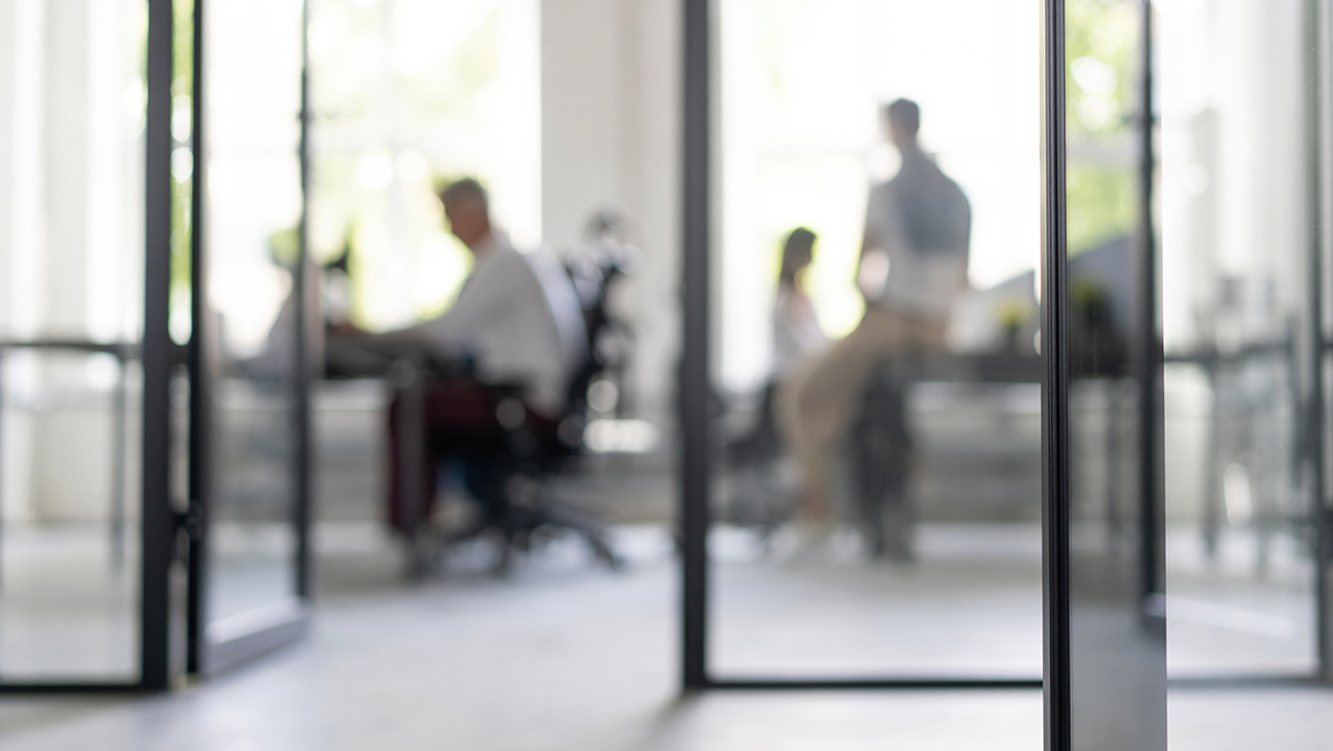 Fyra personer sitter och står i ett kontorsmötesrum, synliga genom glasväggar.