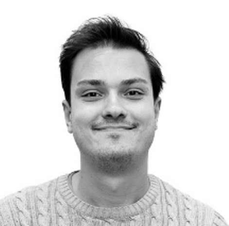 En ung man med kort mörkt hår och ett svagt leende, iförd en ljus stickad tröja, står framför en vit bakgrund.