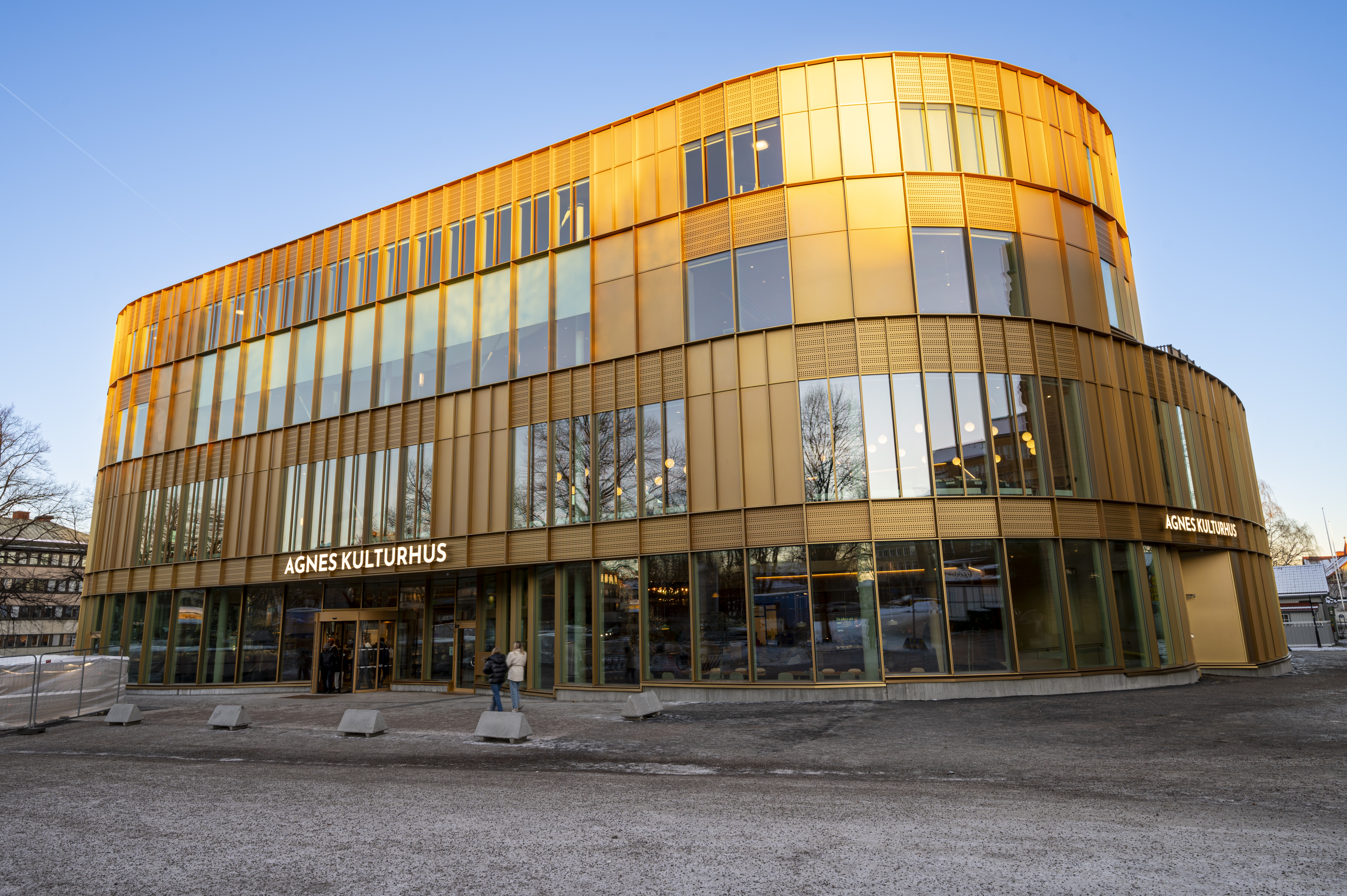 En trevåningsbyggnad med guldfasad och stora glasfönster, märkt "Agnes Kulturhus" vid entrén, fotograferad i dagsljus.