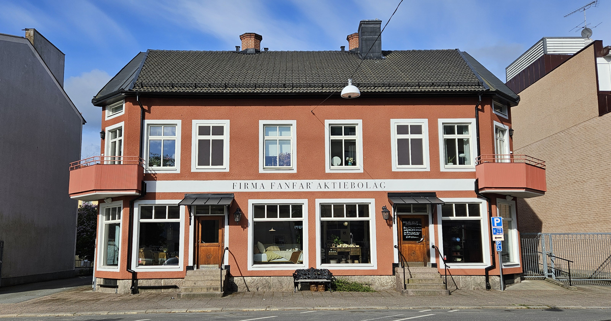 En röd byggnad med två våningar och vita detaljer, märkt "Firma Fanfar Aktiebolag", har stora fönster och två balkonger per sida.