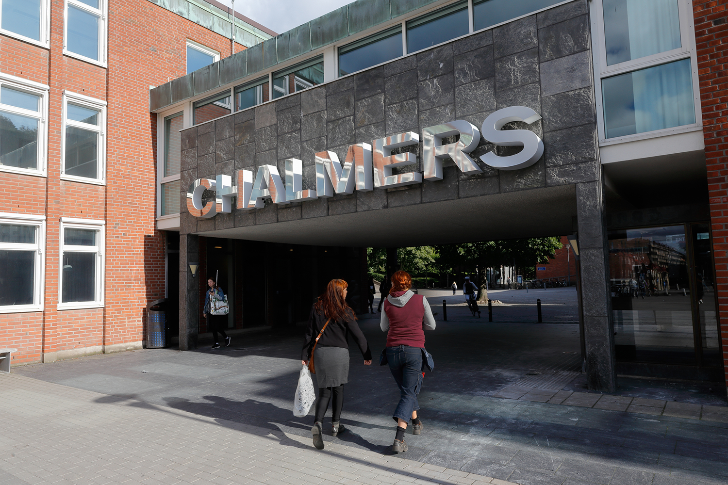 Två personer går mot en ingång med stora metallbokstäver som bildar ordet "CHALMERS" på en byggnadsfasad.