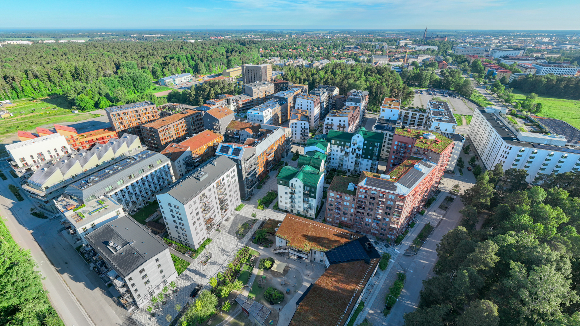 Flygfoto över ett bostadsområde med flerbostadshus omgivna av träd och grönområden under en klar dag.