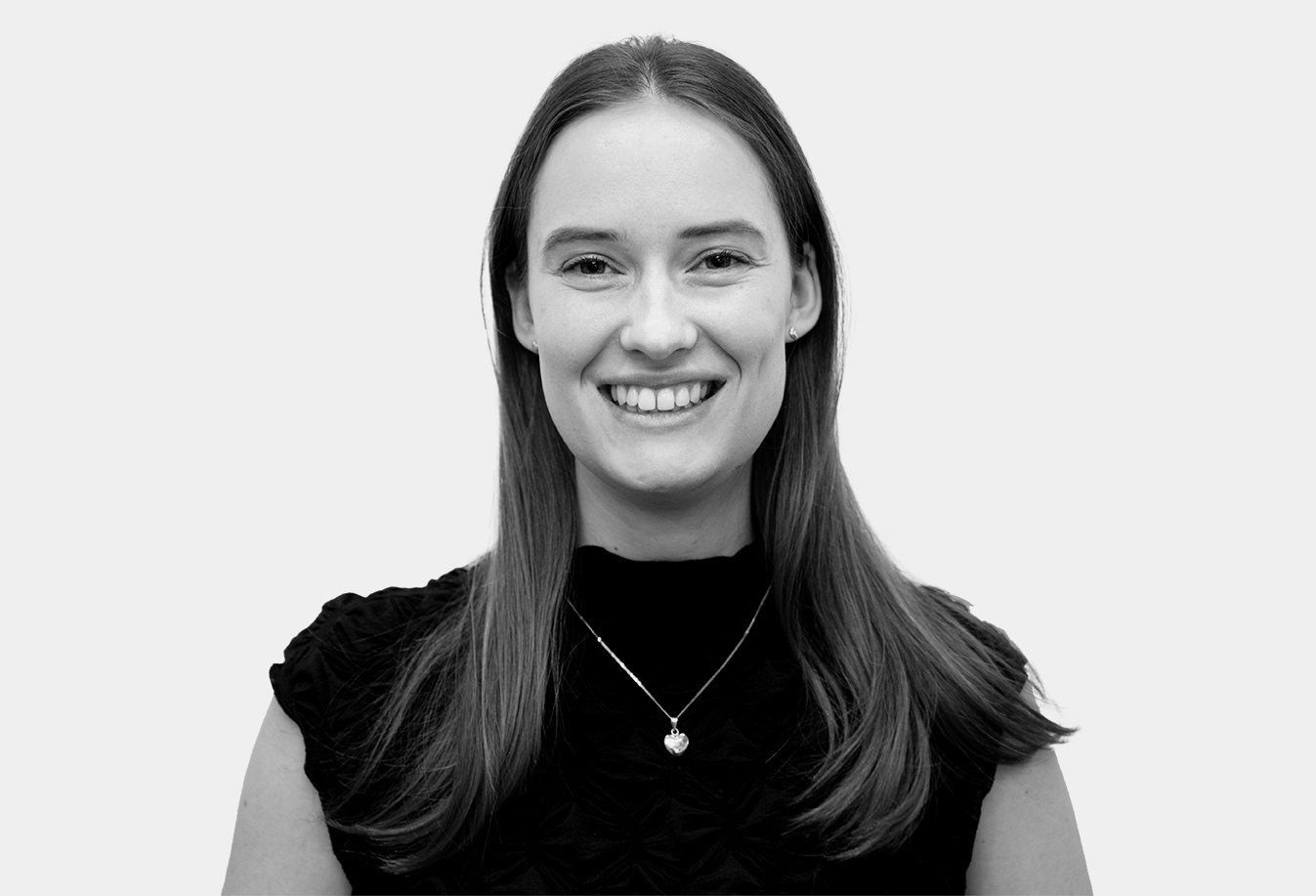 En kvinna med rakt axellångt hår har en mörk kortärmad topp och ett halsband, ler mot kameran mot en ljus bakgrund.