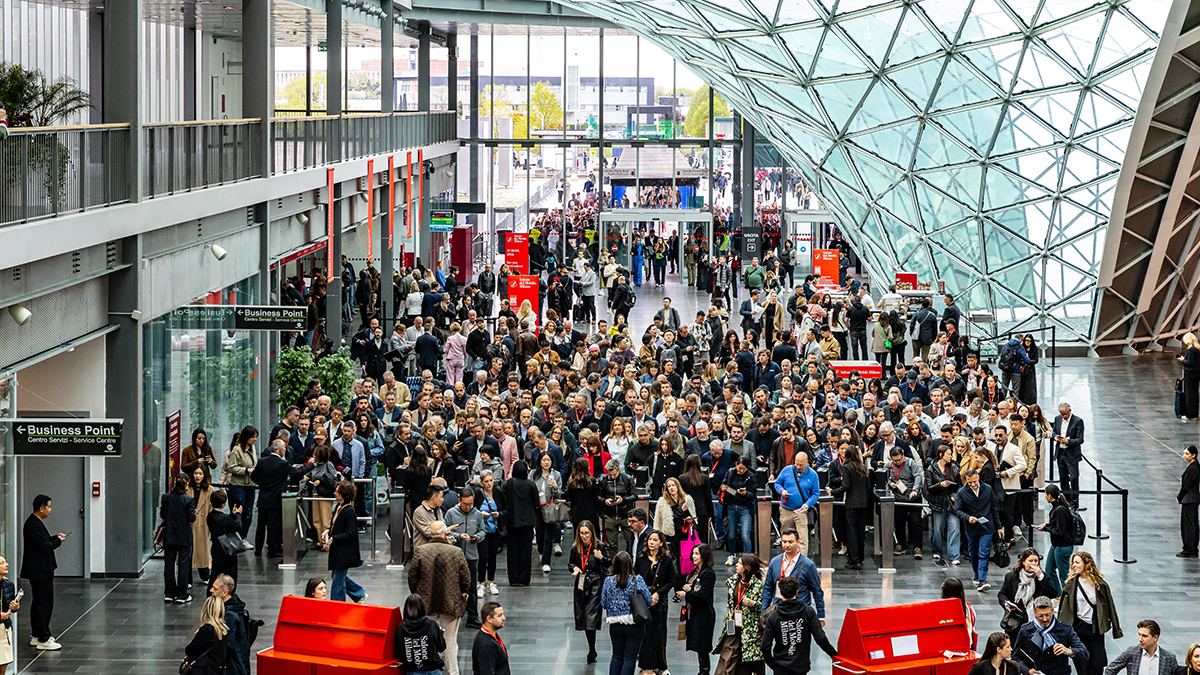 Många personer är samlade i en mässhall med glasväggar. Röda kiosker syns längst fram på bilden.
