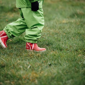 Person som går på gräs bär gröna byxor och röda stövlar.
