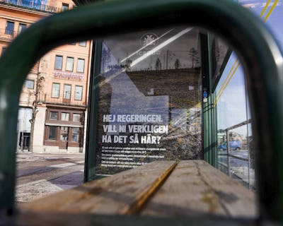 En affisch med text sett genom den böjda metallstrukturen på en busshållplats.