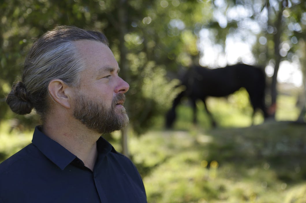 Emil V Nilsson tittar åt sidan med en häst i bakgrunden.