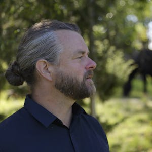 Emil V Nilsson tittar åt sidan med en häst i bakgrunden.