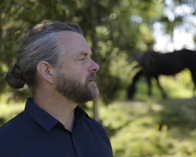 Emil V Nilsson tittar åt sidan med en häst i bakgrunden.