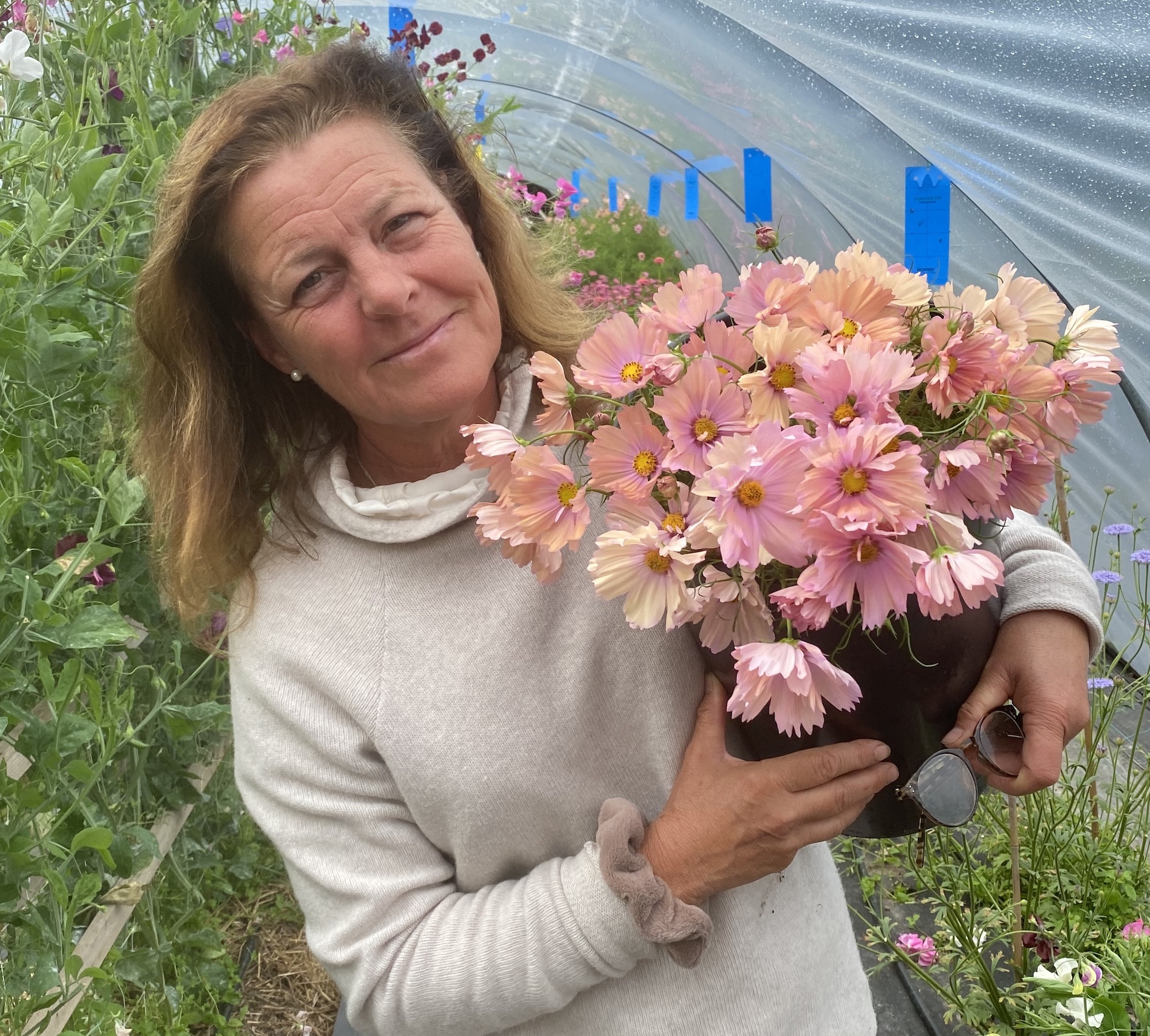 En kvinna som håller en bukett med rosa blommor i växthusmiljö.