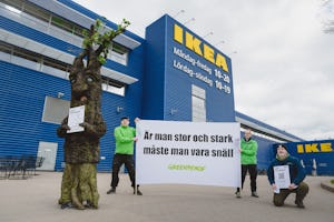 Aktivister klädda som träd håller en banderoll utanför en ikeabutik under en miljöprotest.