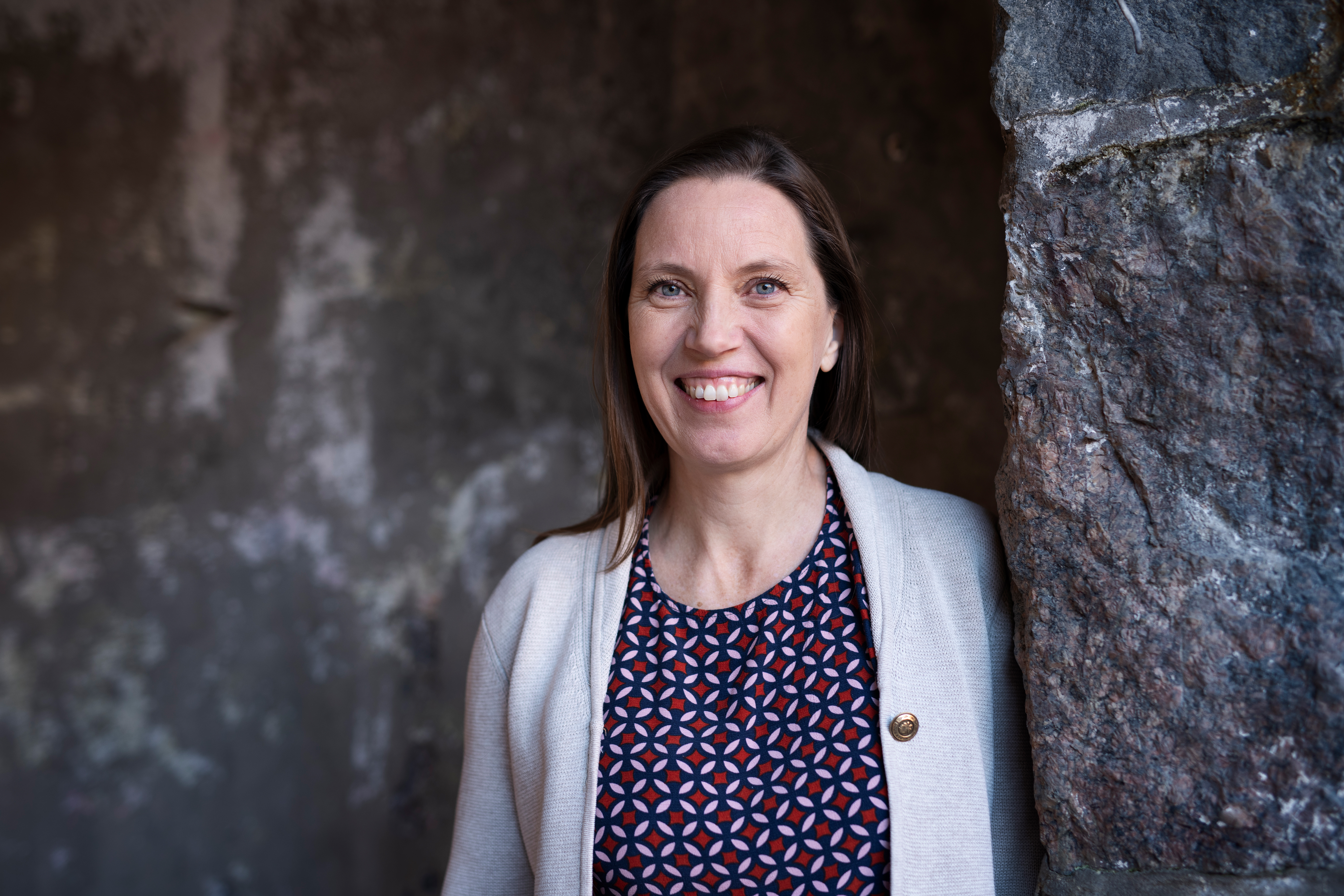 Unn Edberg står bredvid en stenmur och ler mot kameran.